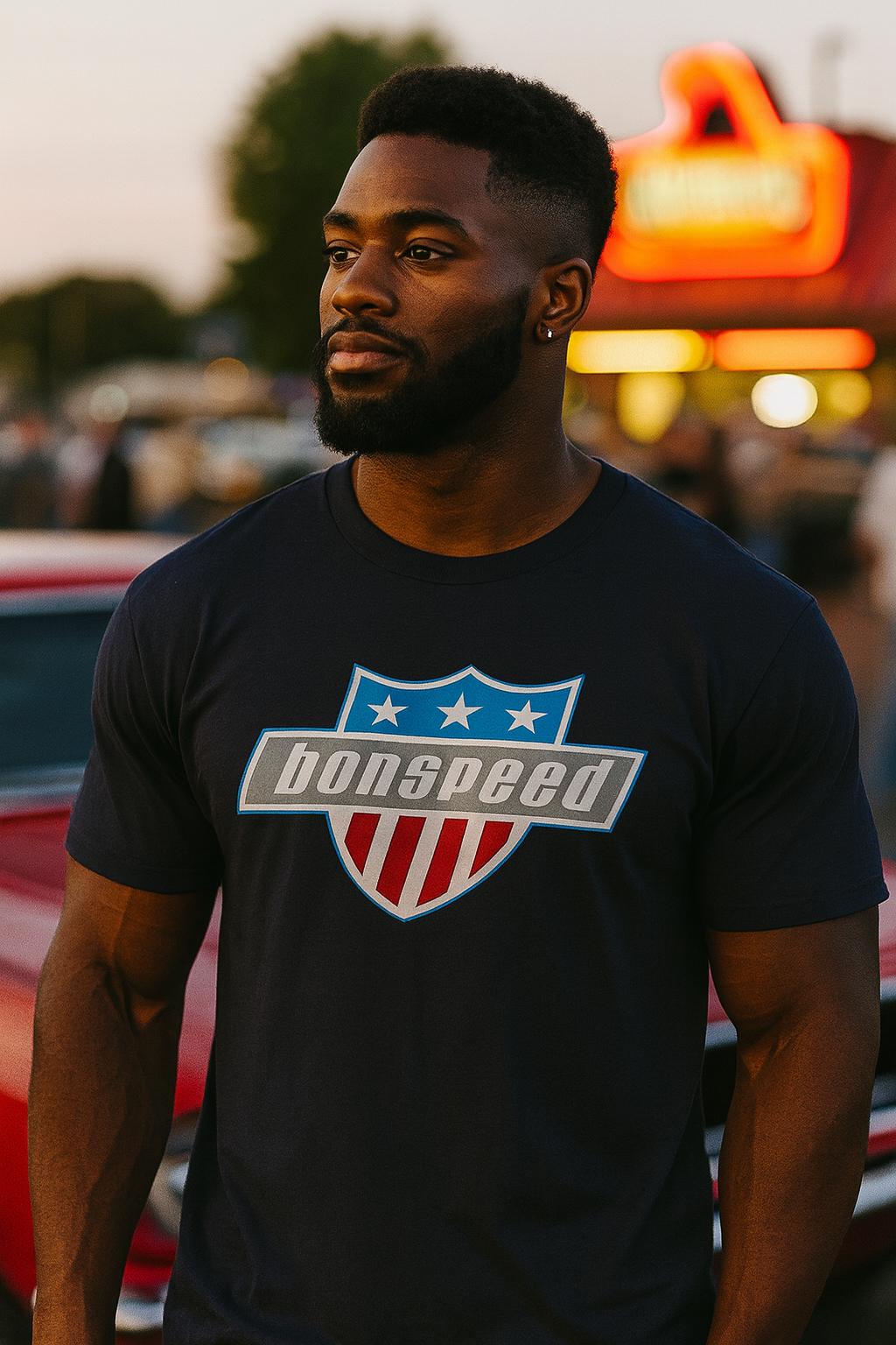 Man wearing a black bonspeed t-shirt with a logo in front of a neon sign.