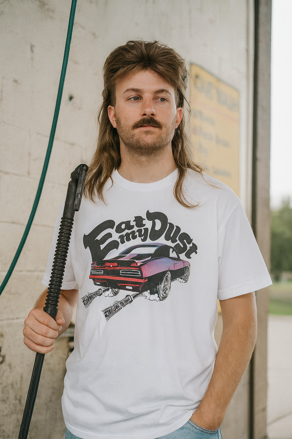 Man wearing a white bonspeed Camaro t-shirt with a graphic design, holding a hose against a wall.