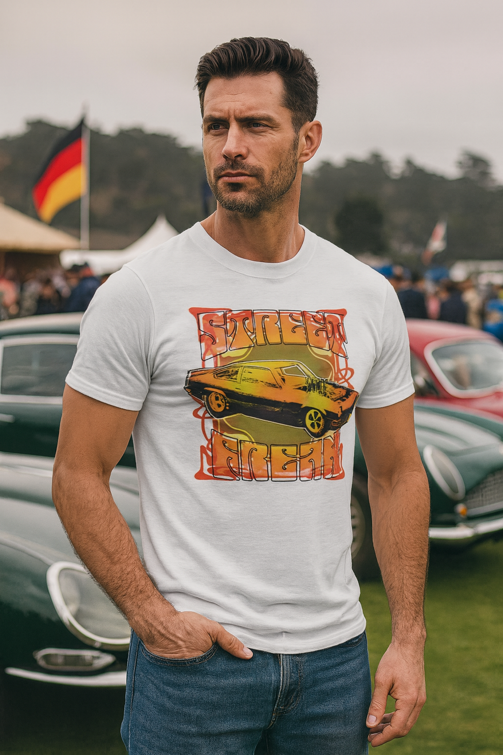 Man wearing a white bonspeed Street Machine t-shirt with a graphic design at an outdoor event with vintage cars.