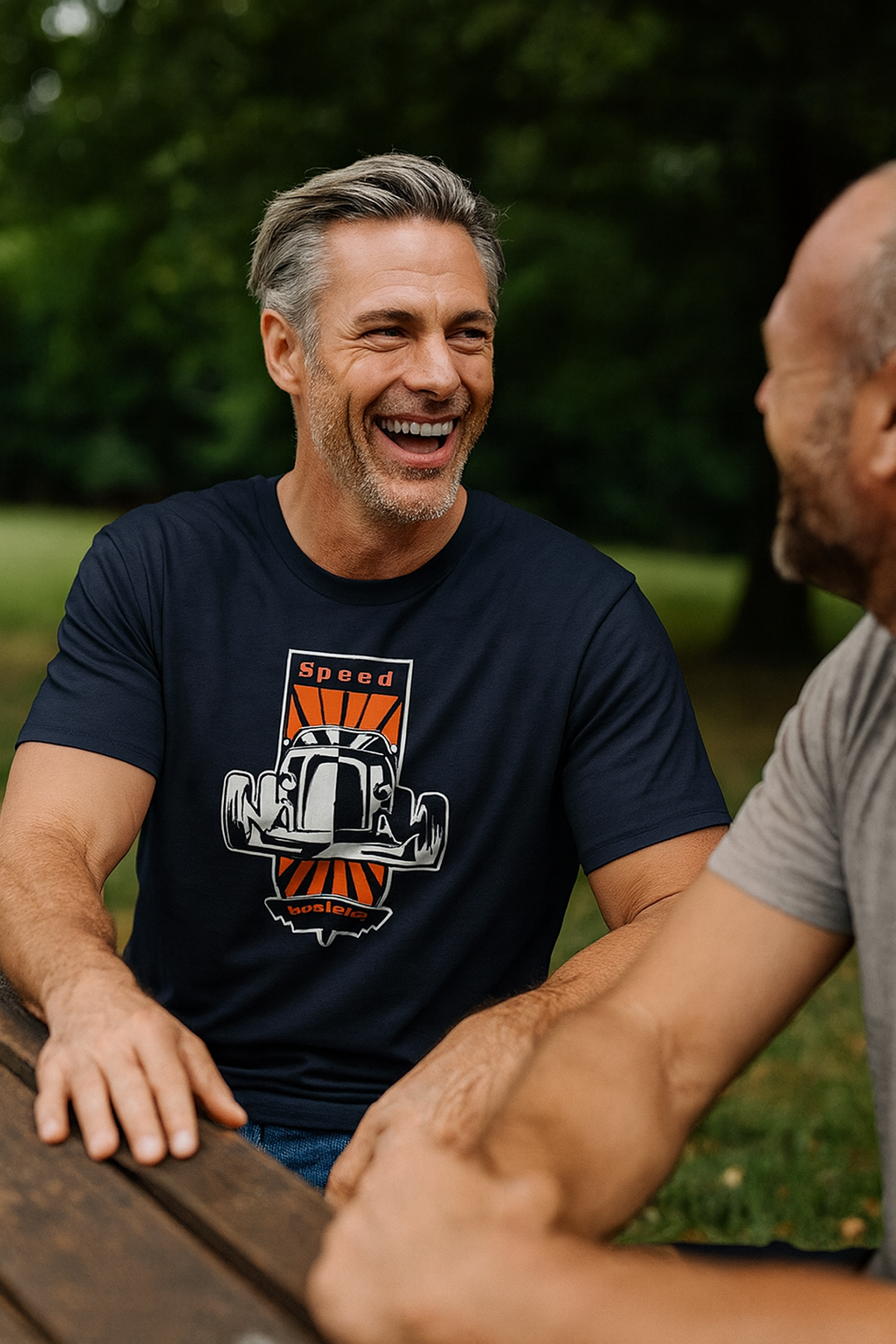 Man wearing a navy blue bonspeed t-shirt with a graphic design, sitting outdoors with another person.