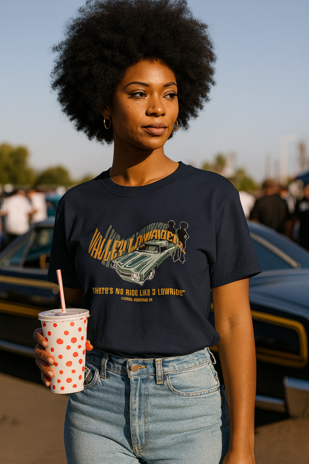 Woman wearing a black t-shirt with a graphic design, holding a cup with a straw, standing outdoors.