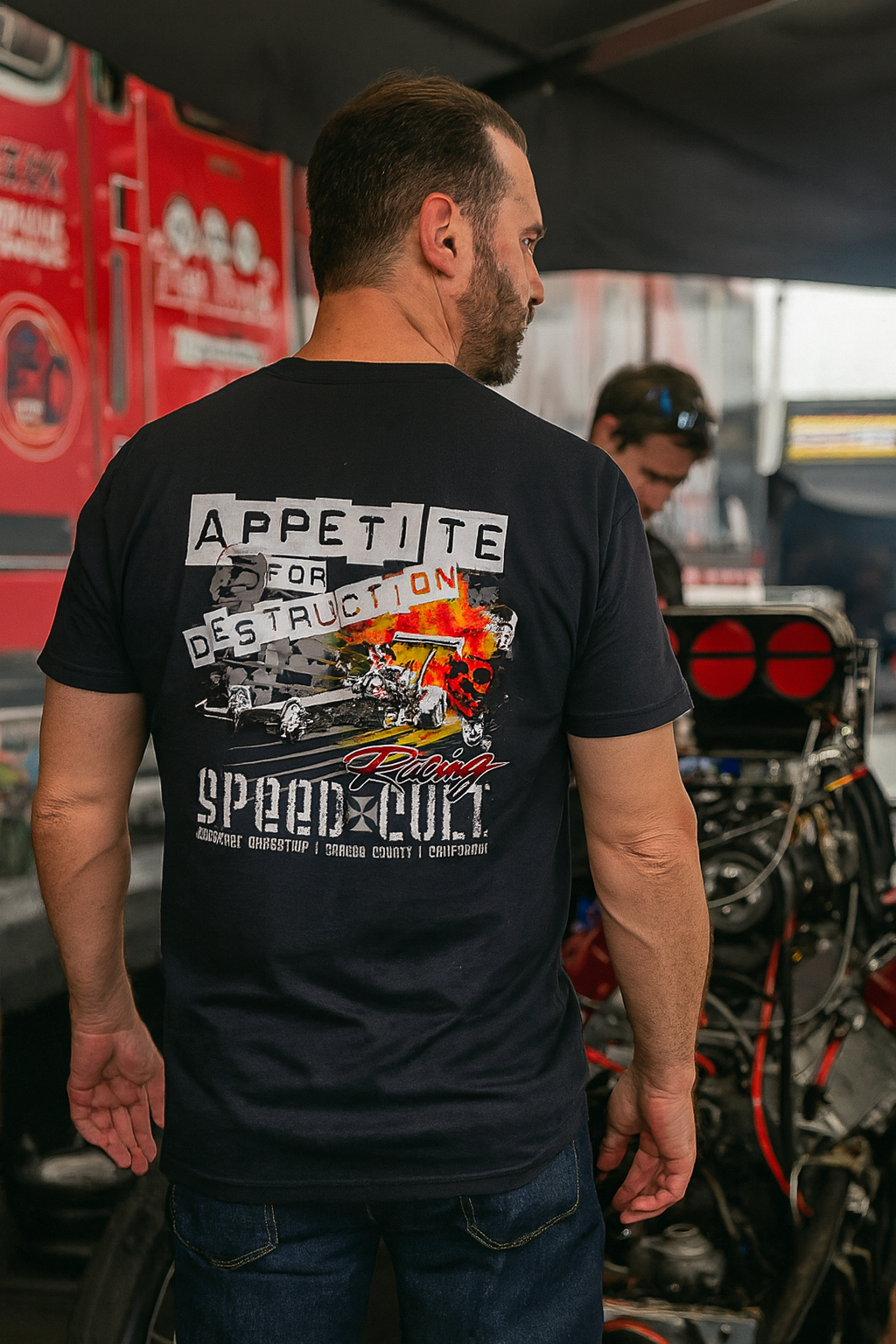 Man wearing a black bonspeed t-shirt with graphic  Top Fuel Dragster design and text, standing in a garage or workshop.
