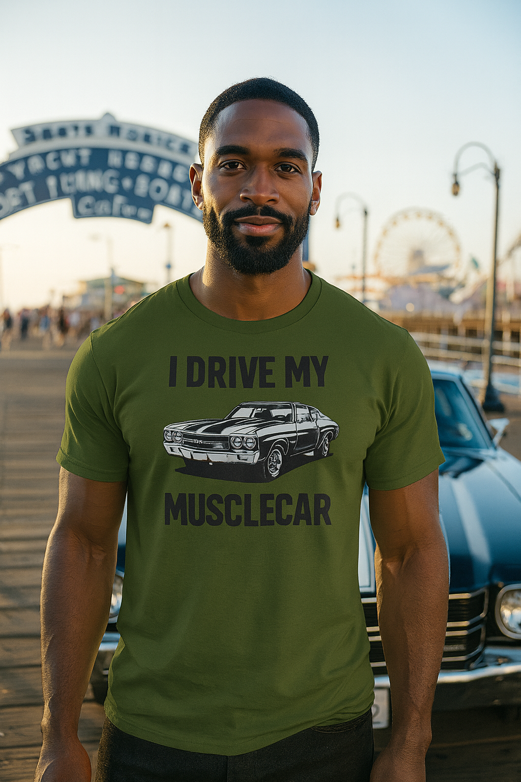 Man wearing a green bonspeed t-shirt with a Musclecar graphic and text, standing in front of a vintage car and boardwalk sign.