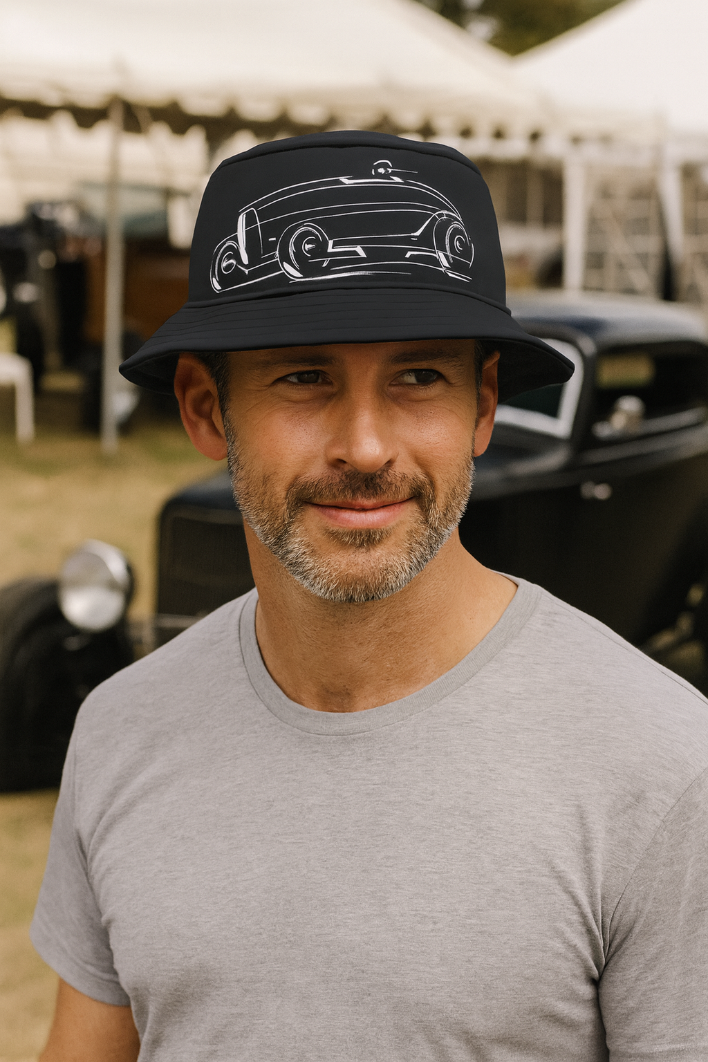 Man wearing a black bucket hat with car design, standing in front of a vintage car.