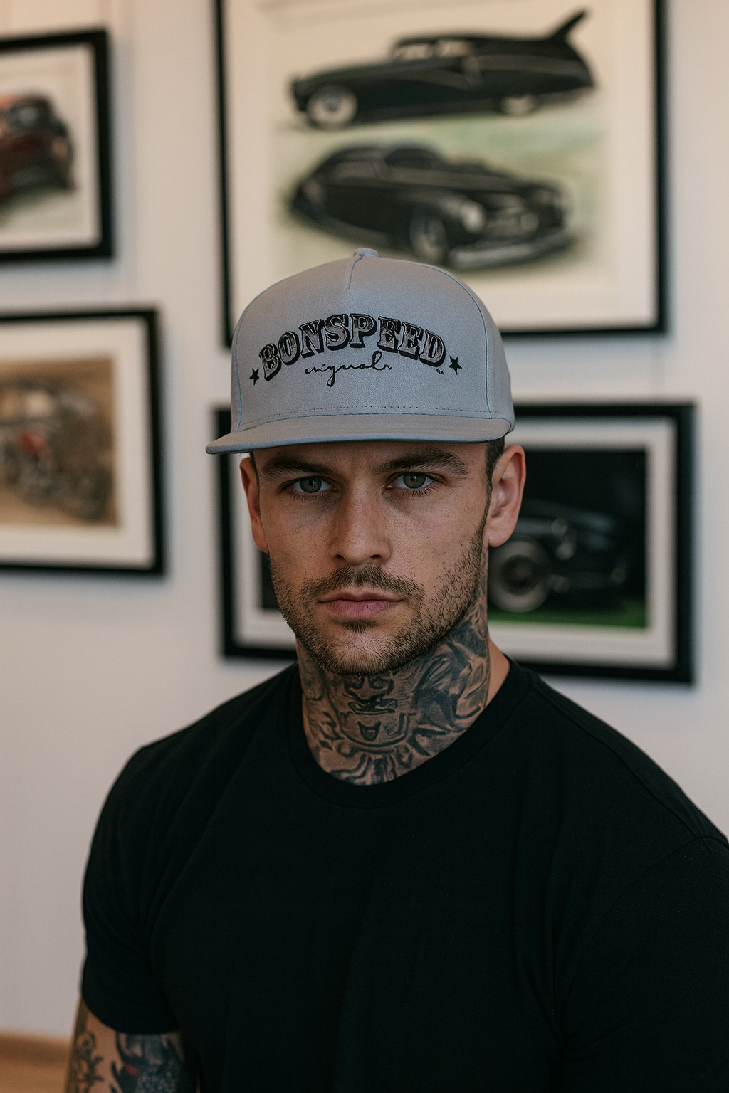 Man wearing a cap with 'Bonspeed' branding in front of framed car pictures.