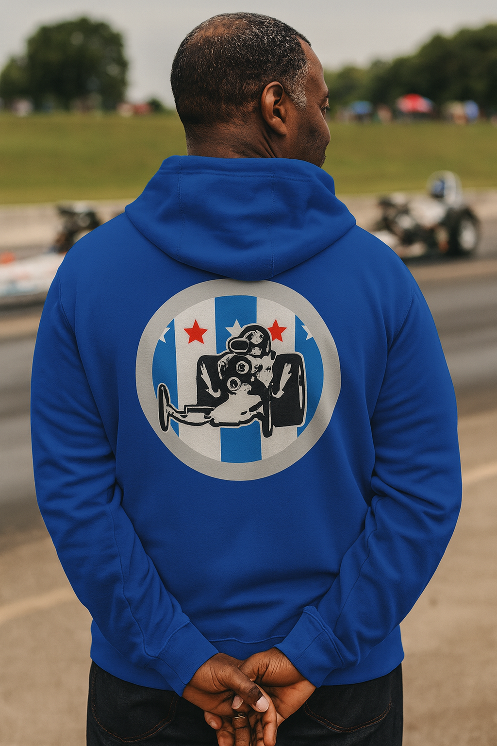 Person wearing a blue bonspeed  hoodie with a graphic dragster on the back, standing on a race track.