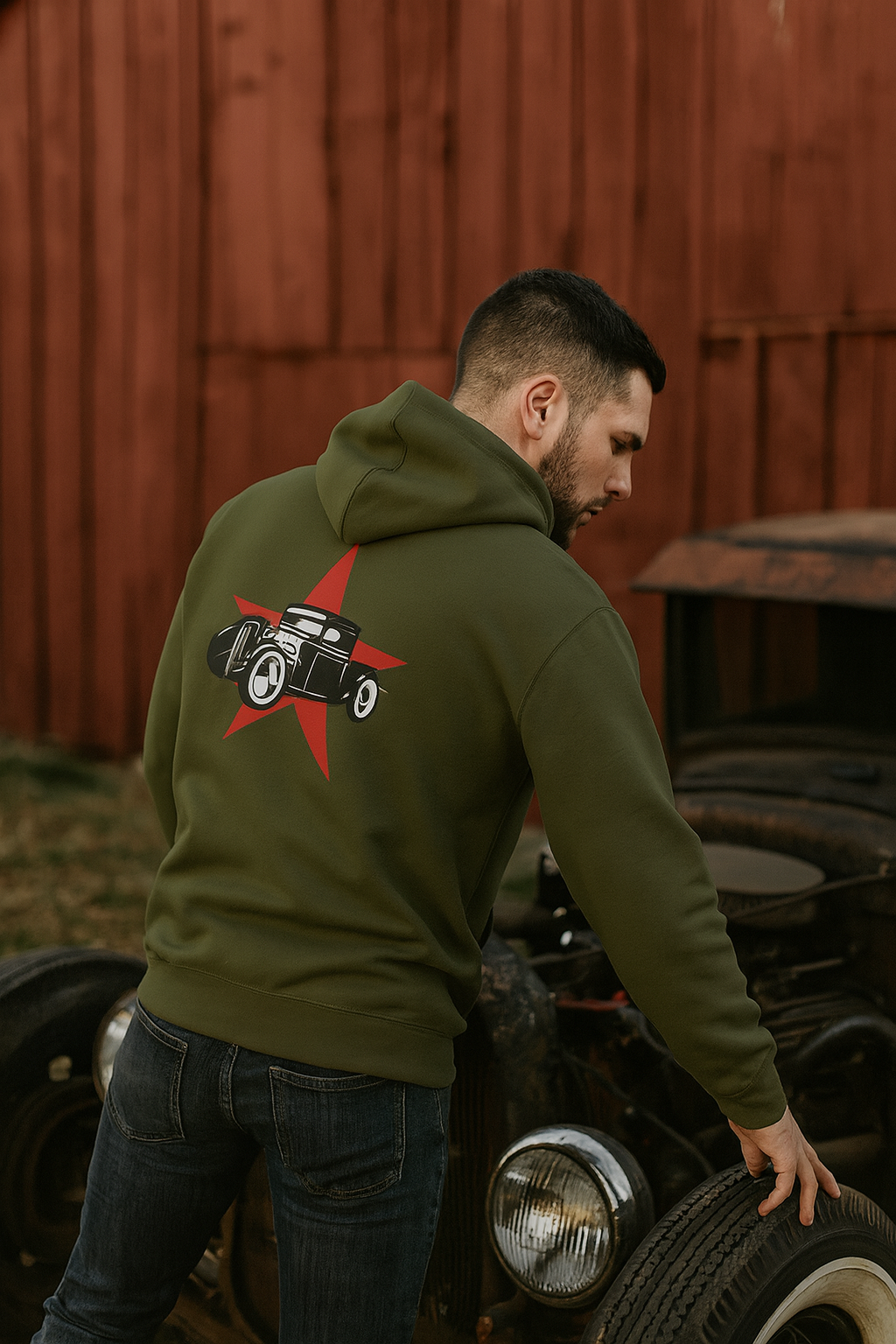 Man wearing a green bonspeed hoodie with a graphic design, standing next to an old car.